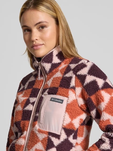 Vrouwenmodel draagt Regular Fit Jacke mit Stehkragen van Columbia, fleece met roze en paarse driehoekpatronen, borstzak met rits, nahaufnahme bovenlichaam