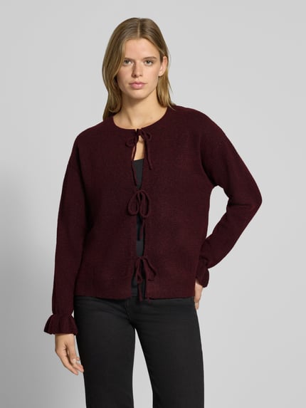 Frauenmodel trägt Strickjacke mit Schleifenverschluss Modell 'PCSALLY' von PIECES in melierter Struktur, Regular Fit, cropped, Ganzkörperansicht von vorne.