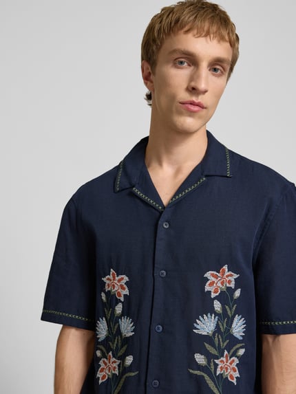 Mannenmodel draagt Relaxed Fit Freizeithemd mit Motiv-Stitching van REVIEW, donkerblauw met bloemendessin, katoenmix, reverskraag, knoopsluiting, halve mouw, detailopname bovenlichaam.