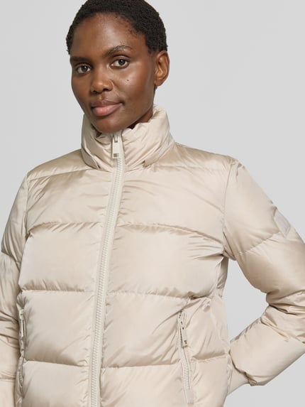 Vrouwenmodel draagt Steppjacke met Daunen-Feder-Füllung van Armani Exchange in beige, elastische materiaalmix, regular fit, opstaande kraag, tweewegritssluiting, ritszakken, capuchon, ruglengte maat S 60 cm, schouderbreedte 41 cm, borstwijdte 50 cm, mouwlengte 62 cm, nahaufnahme bovenlichaam.