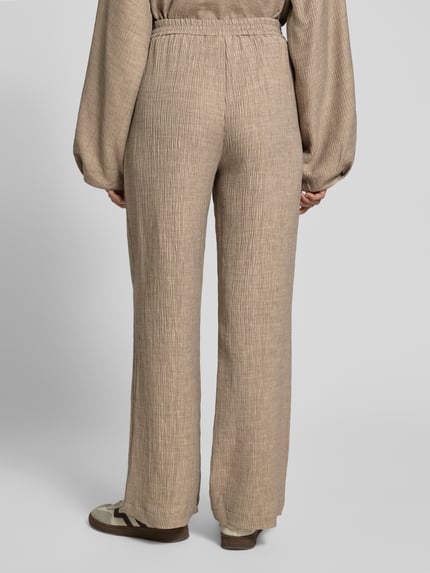 Frauenmodel trägt Stoffhose aus Viskose-Mix mit elastischem Bund von YAS, beige, Wide Leg, strukturierte Oberfläche, Ganzkörperansicht Rückansicht. Modell 'RINA', Stretch-Anteil, Bundweite 38 cm, Innenbeinlänge 78 cm, Größe 36.