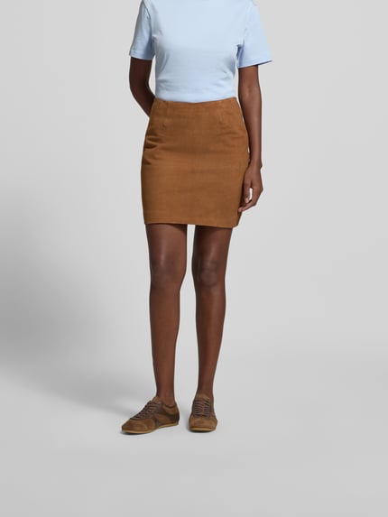 Vrouwenmodel draagt Minirok uit echt chevreau-suède van ROTATE in cognac, slim fit, structuurpatroon, naadritssluiting, suèdelook, totale lengte maat 36: 43 cm, bandwijdte maat 36: 35 cm. Ganzkörperaanzicht van voren.