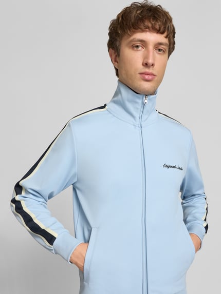 Männermodel trägt hellblaue Sweatjacke mit Stehkragen Modell 'COTEDAZUR' von Jack & Jones, Slim-Fit, Label-Stitching und Reißverschluss, Ganzkörperansicht von vorne. Herren Sweatjacke, Rückenlänge bei Größe M 70 cm, Ärmellänge 65 cm.