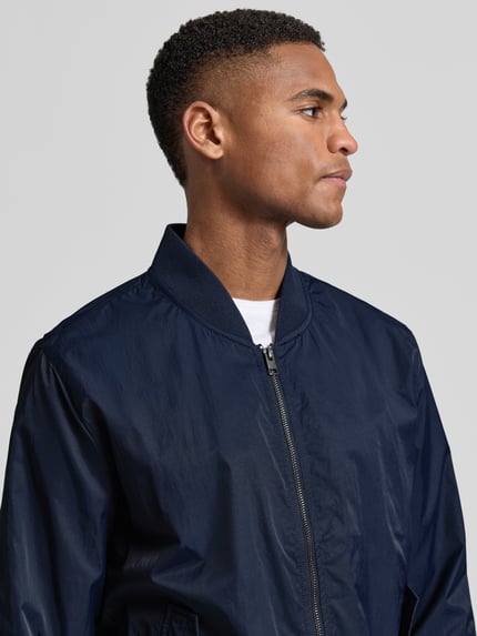 Mannenmodel draagt Regular Fit Bomberjacke mit Stehkragen van s.Oliver RED LABEL in effen donkerblauw met rits, geribde boorden, zijflapzakken en binnenzak, close-up bovenlichaam vooraanzicht.