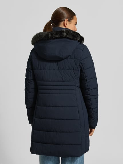 Frauenmodel trägt Jacke mit abnehmbarer Kapuze Modell 'ECLIPSE' von NAUTGÅRD in Dunkelblau, gesteppte Struktur, Ganzkörperansicht Rückansicht. Gerader Schnitt, Zweiwege-Reißverschluss, Label-Patch, seitliche Eingrifftaschen mit Druckknopfverschluss, gestrickte Ärmelabschlüsse, Rückenlänge 79 cm, Schulterbreite 38 cm, Brustweite 48 cm, Ärmellänge 62 cm.