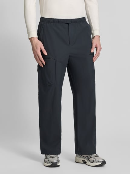 Mężczyzna nosi Regular Fit Hose mit Reißverschlusstaschen von Peak Performance w kolorze ciemnoszarym, elastyczny pas, Szerokość w rozmiarze M: 40 cm, Długość wewnętrzna nogawki w rozmiarze M: 76 cm, Ganzkörperansicht z przodu.