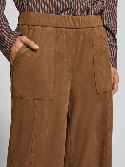 Frauenmodel trägt Regular Fit Lederhose mit großen Taschen von OPUS PANTS in Braun, unifarben, strukturierte Oberfläche, seitliche Eingrifftaschen, Teilungsnähte, elastischer Bund, 7/8-Länge, Nahaufnahme Oberkörper.