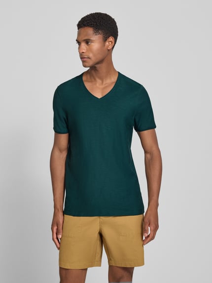 Männermodel trägt T-Shirt mit V-Ausschnitt und Rollsaum von MCNEAL in Dunkelgrün aus Reine Baumwolle, Regular-Fit, Ganzkörperansicht von vorne. Rückenlänge bei Größe M: 81 cm.