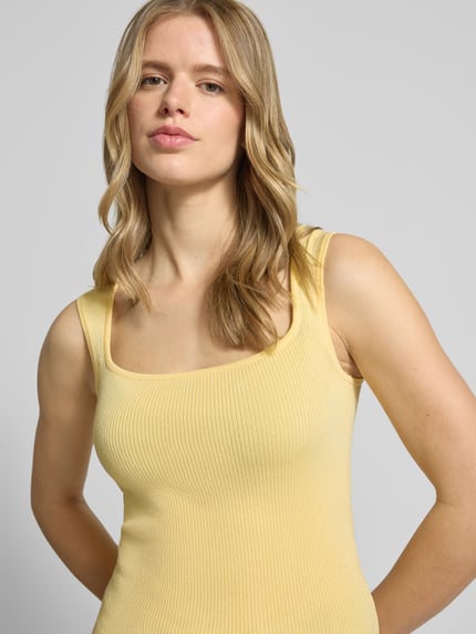 Frauenmodel trägt Top aus Viskose-Mix mit Karree-Ausschnitt Modell 'POSIE' von JJXX, Slim-Fit, gelb, Struktur mit feiner Rippung, Nahaufnahme Oberkörper. Rückenlänge bei Größe S: 52 cm.