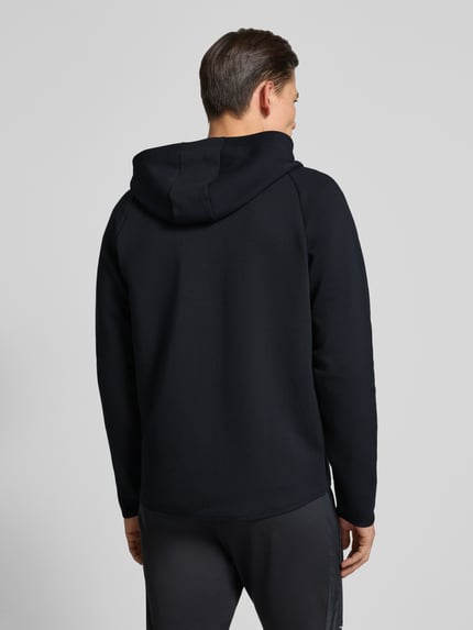Männermodel trägt Trainingsjacke mit Zweiwege-Reißverschluss Modell 'Unstoppable' von Under Armour in Schwarz, Material-Mix, Regular-Fit, Kapuze, Rückenlänge 71 cm, Ärmellänge 60 cm, Ganzkörperansicht Rückansicht.