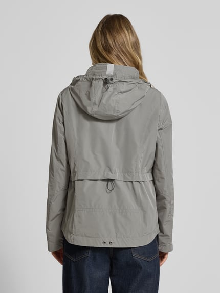Frauenmodel trägt Jacke mit Kapuze und Eingrifftaschen von Gil Bret in Grau, krój regular fit, listwa guzikowa, kieszenie zapinane na zamek błyskawiczny, weather protection, długość tyłu w rozmiarze 36: 67 cm, szerokość ramion w rozmiarze 36: 40 cm, szerokość klatki piersiowej w rozmiarze 36: 46 cm, długość rękawów w rozmiarze 36: 64 cm, gładka tekstura, prostokątne formy, ganzkörperansicht rückansicht.