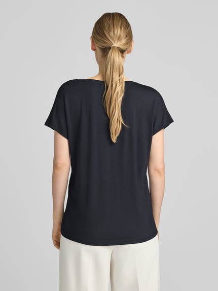 Frauenmodel trägt T-Shirt aus Viskose-Elasthan-Mix mit V-Ausschnitt von Christian Berg Woman in Dunkelblau, Rückenansicht Ganzkörperansicht. Relaxed Fit, Kappärmel, Rückenlänge S: 63 cm, glatte Oberfläche.