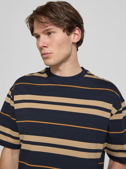 Männermodel trägt Oversized Shirt aus reiner Baumwolle Modell 'NIVARSI' von HUGO in navy-beige gestreift für Herren, Nahaufnahme Oberkörper.