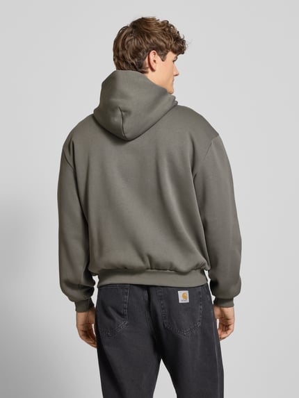 Männermodel trägt Hoodie mit Label-Print und Känguru-Tasche von KARL KANI in Oliv, Baumwoll-Mix, oversized, Ganzkörperansicht Rückansicht.