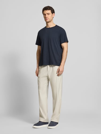 Männermodel trägt Regular Fit T-Shirt aus reiner Baumwolle Modell 'HASPEN' von SELECTED HOMME in Melange-Optik mit Rundhalsausschnitt, kurzarm, kombiniert zu heller Hose, Farbkontrast zwischen Dunkelblau und Beige, Ganzkörperansicht von vorne.