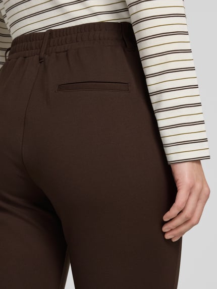 Frauenmodel trägt Loose Fit Bundfaltenhose aus Viskose-Mix von Tom Tailor in Dunkelbraun, glatte Textur, Nahaufnahme Hüfte, Damen Bundfaltenhose von Tom Tailor.