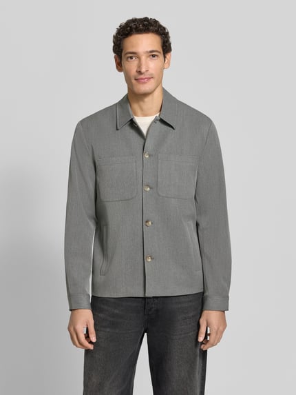 Männermodel trägt Hybrid Jacke mit Brusttaschen Modell 'Marseille' von Les Deux in Grau, Kentkragen, Knopfleiste, Ganzkörperansicht von vorne.