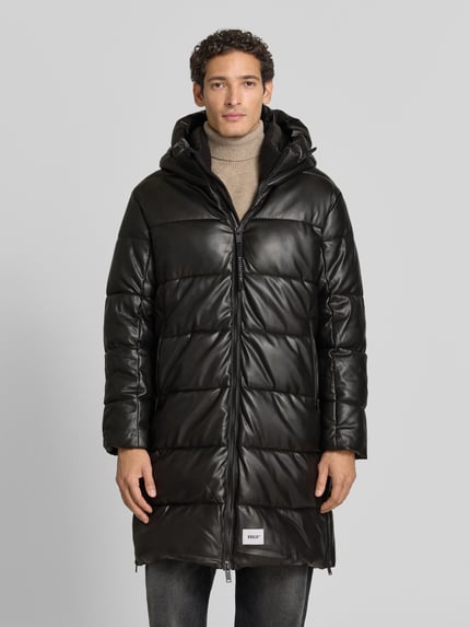 Männermodel trägt Regular Fit Mantel in Stepp-Optik Modell 'EMMET' von khujo in Schwarz, glatte Textur, Ganzkörperansicht von vorne.