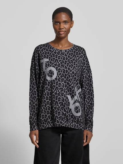 Frauenmodel trägt Oversized Strickpullover im Allover-Look von Smith and Soul, Baumwoll-Mix, Rundhalsausschnitt, schwarze Grundfarbe, animalischer Musterprint, dezente graue Akzente, locker geschnitten, Ganzkörperansicht von vorne.