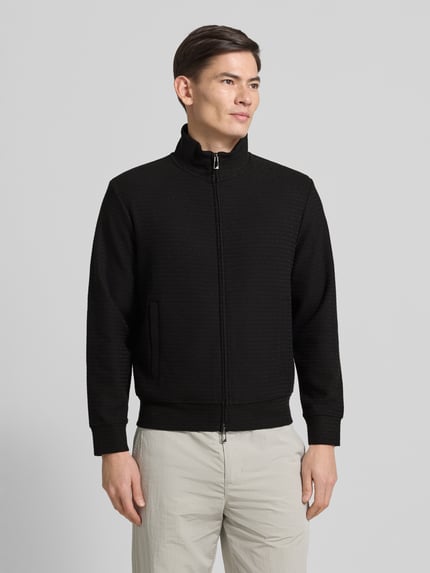 Männermodel trägt Sweatjacke mit Stehkragen von Emporio Armani, Schwarz, Baumwoll-Lyocell-Mix mit Stretch-Anteil, lockerer Schnitt, Reißverschluss, Eingrifftaschen, gerippte Abschlüsse, Rückenlänge 64 cm, Ärmellänge 60 cm, Ganzkörperansicht von vorne.