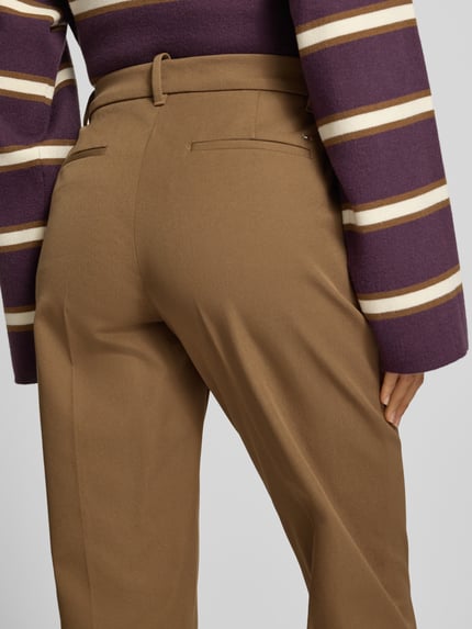 Frauenmodel trägt Regular Fit Stoffhose mit Bügelfalten von T. HILFIGER SPW., schmale unifarbene Hose mit feinem Webstruktur-Muster, seitliche Eingrifftaschen und Gesäßtaschen, Bundfalte, Gürtelschlaufen, Detailaufnahme Rückansicht.