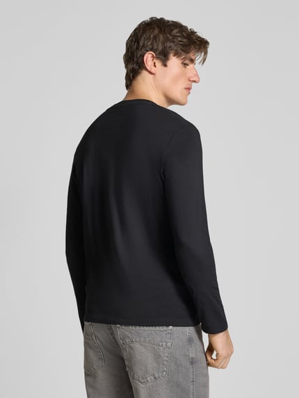 Männermodel trägt Langarmshirt mit dezentem Logo-Detail von S.OLIVER CASUAL in Schwarz, dezente Struktur, Unifarbe, Ganzkörperansicht Rückansicht.