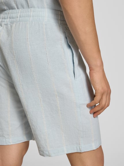 Männermodel trägt Leinenshorts mit Logo-Stitching von REVIEW, hellblauer Baumwoll-Mix mit Leinen-Anteil, Nahaufnahme Oberschenkel.