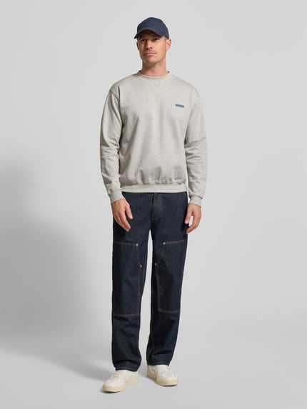 Männermodel trägt Sweatshirt mit Label-Print Modell 'Cane' von WOODBIRD aus Bio-Baumwolle, hellgrau, Regular Fit, Ganzkörperansicht von vorne.