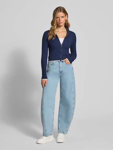 Frauenmodel trägt Slim Fit Strickjacke aus Viskose-Mix von Tommy Jeans in Dunkelblau zu hellblauer Jeans, Ganzkörperansicht von vorne, Damen Strickjacke von Tommy Jeans.