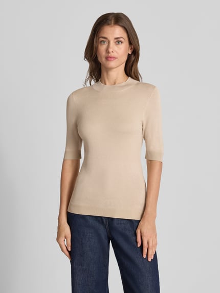 Frauenmodel trägt Slim Fit Strickpullover aus Viskose-Mix von COMMA in Beige, gerippte Abschlüsse, Halbarm, Ganzkörperansicht von vorne.
