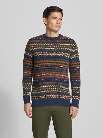 Männermodel trägt Pullover mit Jacquardstruktur von BARBOUR, buntes geometrisches Allover-Muster, Strickoptik, Ganzkörperansicht von vorne.