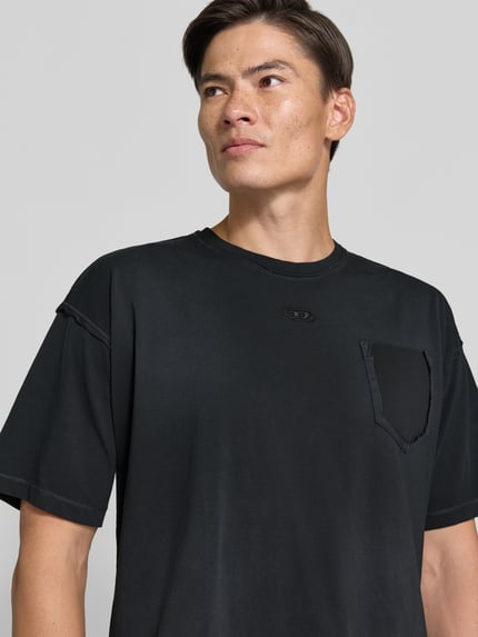 Männermodel trägt schwarzes T-Shirt mit Label-Stitching von Diesel aus reiner Baumwolle und Brusttasche, Nahaufnahme Oberkörper.