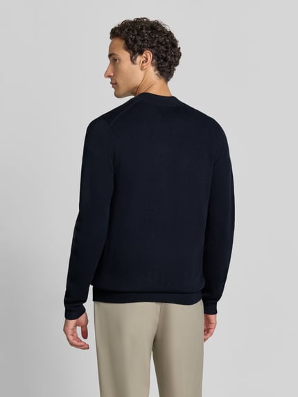 Männermodel trägt Slim Fit Strickjacke aus Baumwoll-Mix mit Stehkragen von Christian Berg Men, dunkelblau, gerippte Abschlüsse, Ganzkörperansicht Rückansicht.