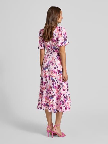 Vrouwenmodel draagt wikkeljurk in midilengte model 'Thea' van YAS met bloemenprint, getailleerde pasvorm, elastische materiaalmix, geheelopname achteraan.