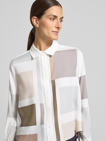 Kobieta nosi Regular Fit Hemdbluse aus Seiden-Mix von HERZENS, geometryczne wzory, jasne beże i biel, krój regular fit, elastyczny jedwabny miks, kołnierzyk koszulowy, długa listwa guzikowa, długie rękawy, długość tyłu w rozmiarze 36: 61 cm, długość rękawa w rozmiarze 36: 64 cm, zdjęcie portretowe, z przodu.