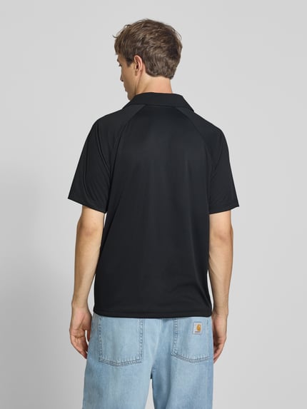Männermodel trägt Relaxed Fit Poloshirt mit Logo-Stitching von Champion in Schwarz, kurze Ärmel, glatte Textur, Jeans, Ganzkörperansicht Rückansicht. Rückenlänge bei Größe M: 70 cm.