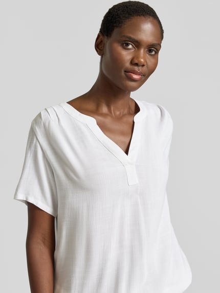 Modelka nosi Regular Fit Bluse aus reiner Viskose von Tom Tailor, efekt: jednolity kolor, krój regular fit, kołnierz z lamówką, dekolt w serek, krótki rękaw, wykończenie: elastyczny, materiał: wiskoza, półzbliżenie górnej części ciała.