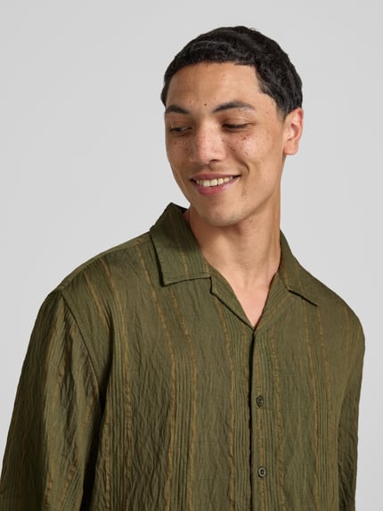 Männermodel trägt Modern Fit Freizeithemd mit Strukturmuster Modell 'Henrik' von Redefined Rebel im grünen Rayon-Mix, Nahaufnahme Oberkörper. Rückenlänge bei Größe M: 72 cm, Schulterbreite: 51 cm, Ärmellänge: 27 cm, Reverskragen, Knopfleiste.