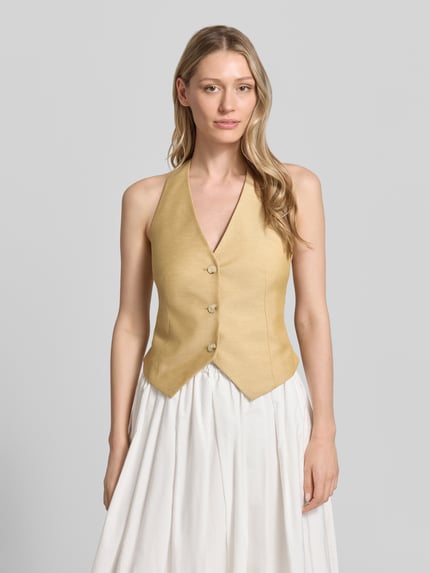 Vrouwenmodel draagt bodywarmer met halter en V-hals van comma, materiaalmix met linnen, getailleerd model, knoopsluiting, ruglengte 21 cm, schouderbreedte 41 cm, borstwijdte 37 cm, lichte kleur, gladde textuur, effen vormgeving, vooraanzicht bovenlichaam