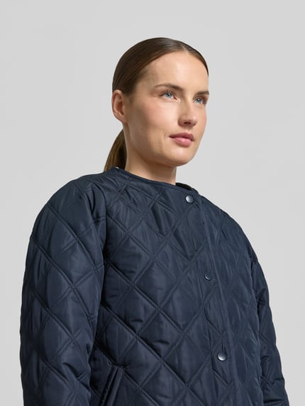 Kobieta nosi Regular Fit kurtkę z efektem pikowania z kapturem model 'Fenya' od Soyaconcept, wpuszczane kieszenie, listwa guzikowa, długość tyłu w rozmiarze S: 65 cm, szerokość ramion w rozmiarze S: 40 cm, szerokość klatki piersiowej w rozmiarze S: 54 cm, długość rękawów w rozmiarze S: 65 cm, ciemnogranatowa, geometryczne pikowanie, zbliżenie na górną część tułowia