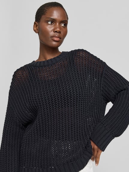 Modelka nosi sweter 'Pullover in Strick-Optik' od Juvia z mieszanki bawełny, półprzezroczysty efekt, krój relaxed fit, okrągły dekolt, długość tyłu w rozmiarze S 67 cm, widok na górną część ciała z przodu