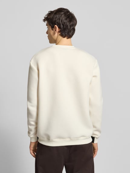 Męski model nosi Sweatshirt mit Label-Print Modell 'CORVARO' od Ellesse, luźny krój, kremowy kolor, ribbingi, widok całej sylwetki od tyłu.