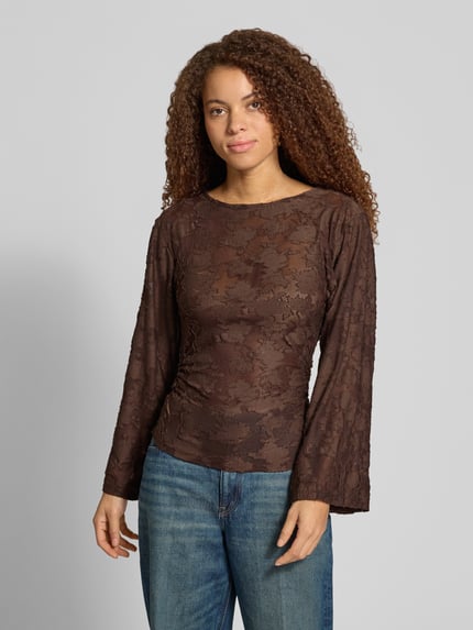 Frauenmodel trägt Langarmshirt mit Mesh Ausbrenner-Effekt von ONLY, brauner Stoff mit Spitzenmuster, abgerundeter Rumpfabschluss, Ganzkörperansicht von vorne.