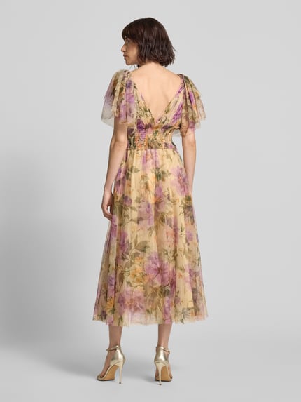 Modelka nosi 'Cocktailkleid mit Smok-Details und V-Ausschnitt' od LACE & BEADS, szyfon, linia A, długość midi, V-dekolt, detale smok, motylkowe rękawy, długość pleców w rozmiarze S: 102 cm, szerokość w rozmiarze S: 38 cm, długość rękawa w rozmiarze S: 17 cm, pastelowe kwiaty na beżowym tle, widok całej sylwetki z tyłu.