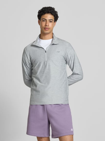 Männermodel trägt Regular Fit Sweatshirt mit Troyer-Kragen von New Balance, leichter Elastischer-Material-Mix, Logo-Print, Ganzkörperansicht von vorne. Rückenlänge bei Größe M: 69 cm.