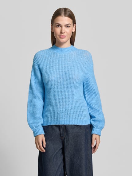 Frauenmodel trägt Pullover mit Ballonärmeln Modell 'Siforo' von HUGO in Hellblau, Strukturstrick, Mock Neck, Rippenabschlüsse, Ganzkörperansicht von vorne.