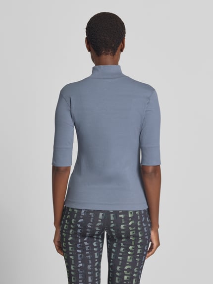 Frauenmodel trägt Slim Fit T-Shirt aus Baumwoll-Mix mit Stehkragen von Marc Cain in Blau, 1/2-Arm, elastisch, Rückenlänge 54 cm, Ganzkörperansicht Rückansicht.