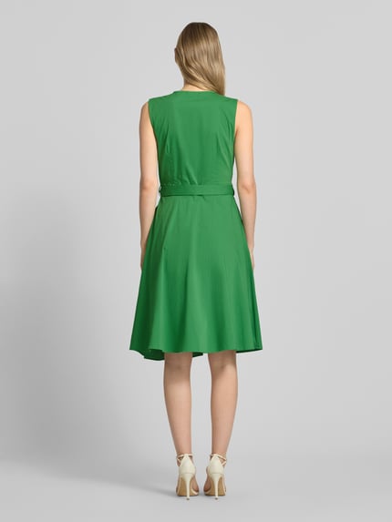 Modelka nosi Kleid mit V-Ausschnitt in Wickel-Optik von More & More, zielony kolor, krój slim fit, bawełniana elastyczna tkanina, zdejmowany pasek, bez rękawów, widok całej sylwetki od tyłu