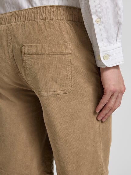 Männermodel trägt Regular Fit Shorts mit Tunnelzug Modell 'Joey' von Redefined Rebel, sztruks, mieszanka bawełny i elastanu, kolor beżowy, szerokość w rozmiarze M: 39 cm, długość wewnętrzna nogawki w rozmiarze M: 25 cm, detal tylnej kieszeni, zbliżenie na tył, zdjęcie szczegółowe
