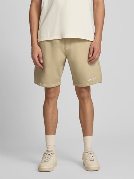 Männermodel trägt Shorts mit elastischem Bund und Logo-Stitching von Pegador aus Baumwoll-Mix, Loose-Fit, Eingrifftaschen, Ganzkörperansicht von vorne.